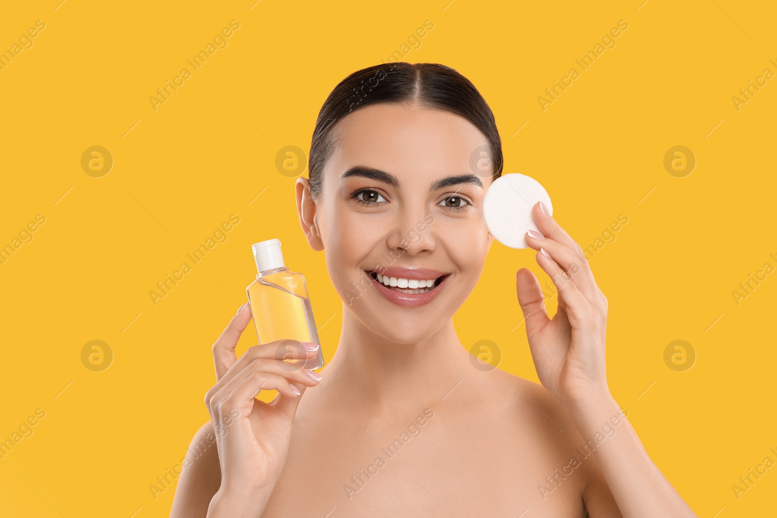 Photo of Beautiful woman holding makeup remover and cotton pad on orange background, space for text