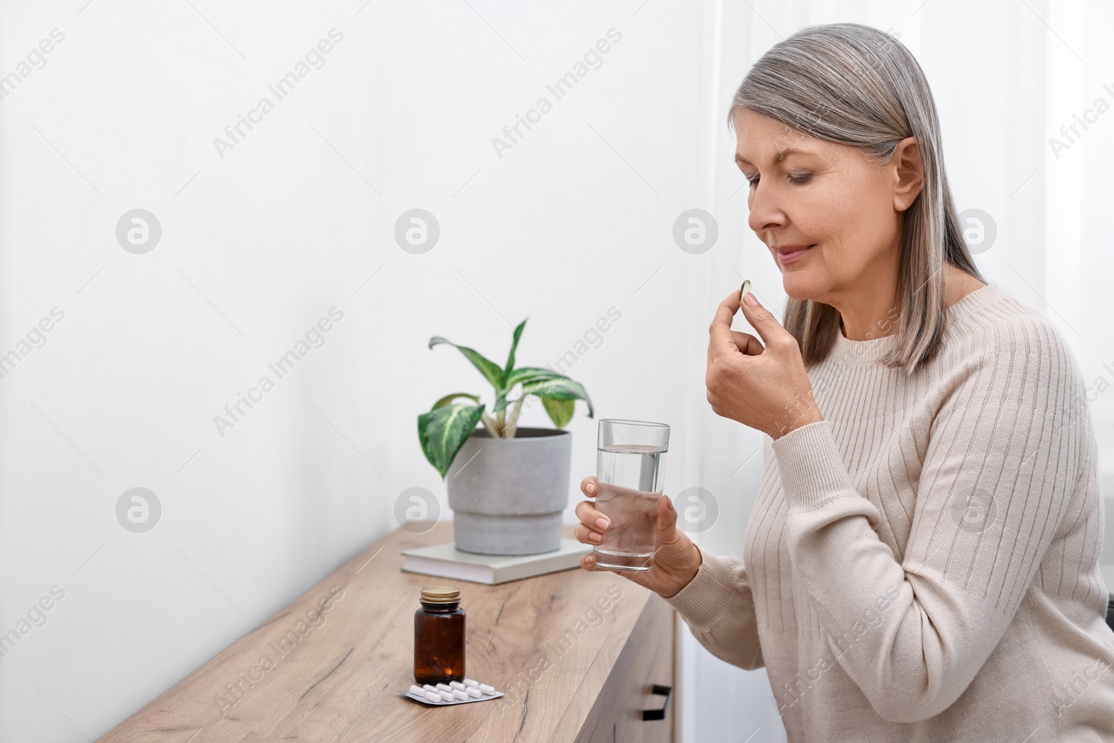 Photo of Beautiful woman taking vitamin pill at table indoors. Space for text