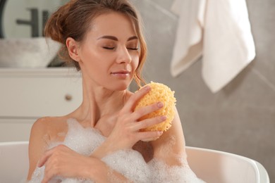 Photo of Beautiful woman with sponge taking bath indoors