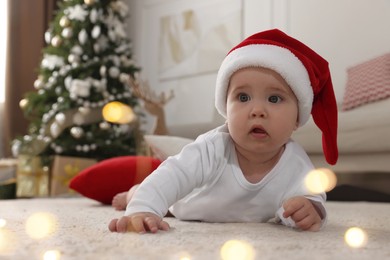 Photo of Baby wearing Santa hat on floor in room decorated for Christmas