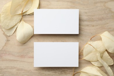 Photo of Blank business cards and beige leaves on wooden table, flat lay. Mockup for design