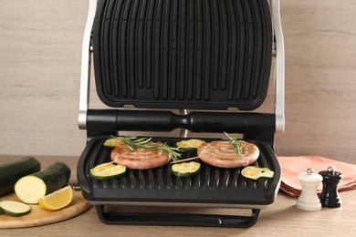 Photo of Electric grill with homemade sausages, zucchini and rosemary on wooden table