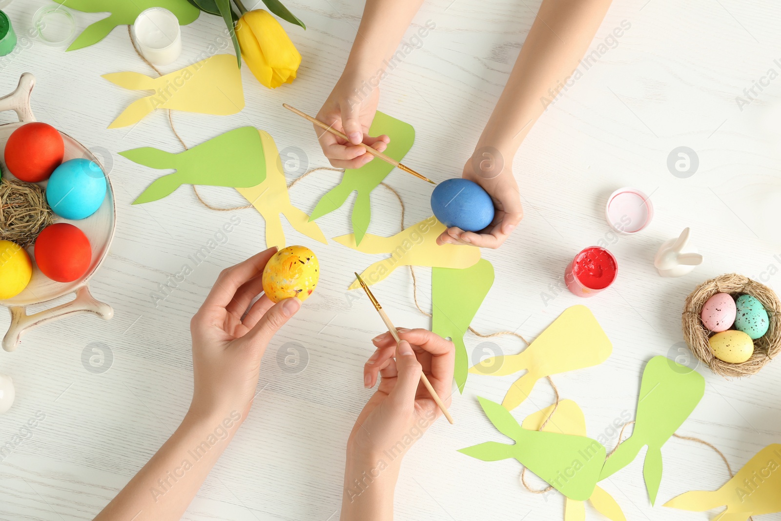 Photo of Mother and her child painting Easter eggs at table, top view