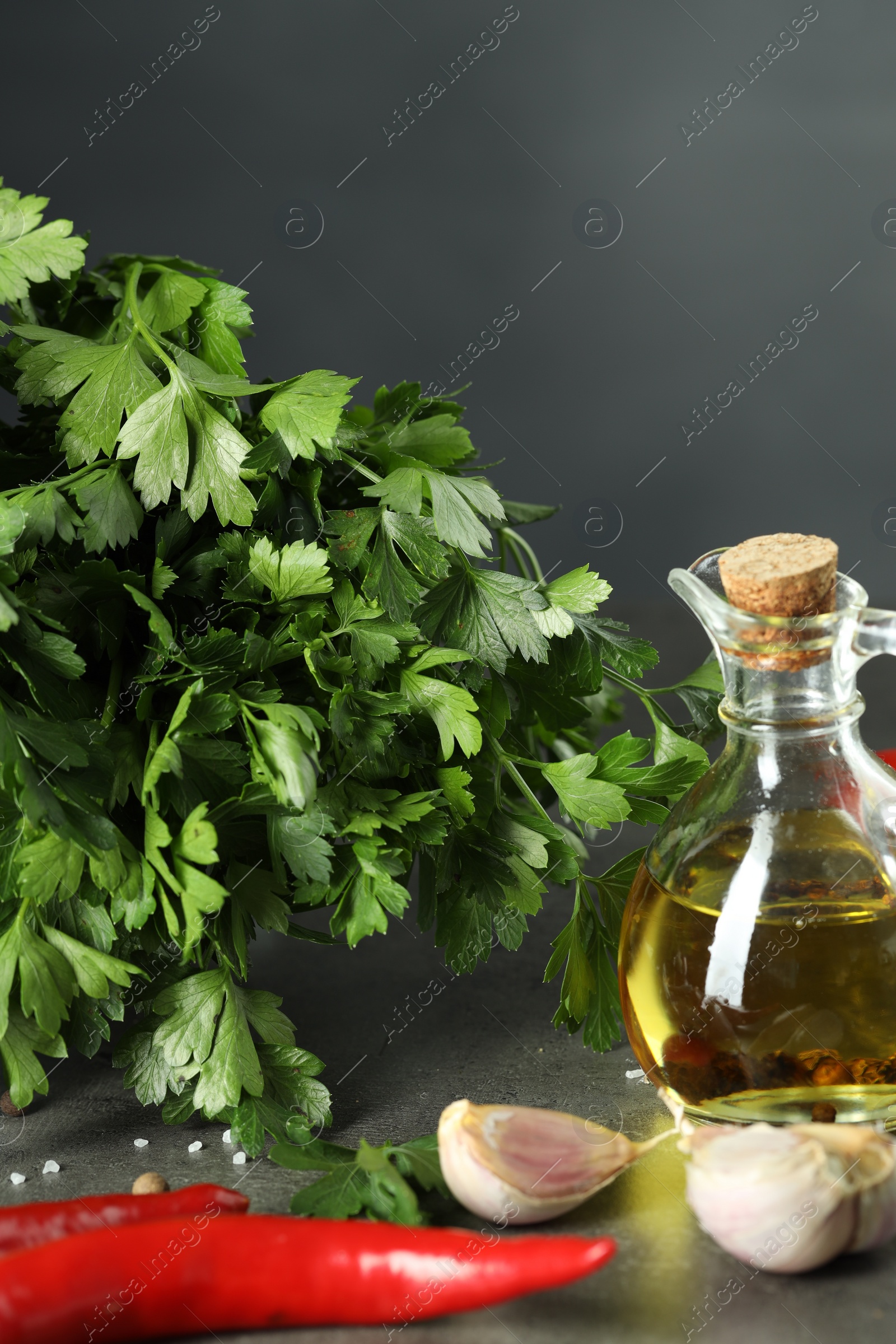 Photo of Fresh parsley, oil and other products on grey table, closeup