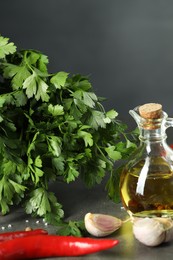 Photo of Fresh parsley, oil and other products on grey table, closeup