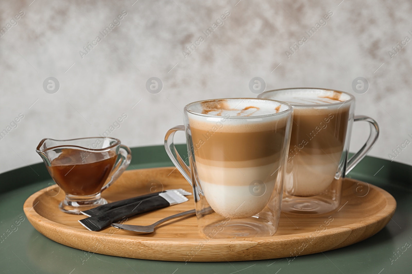 Photo of Tray with glass cups of caramel macchiato and syrup in gravy boat on table. Space for text