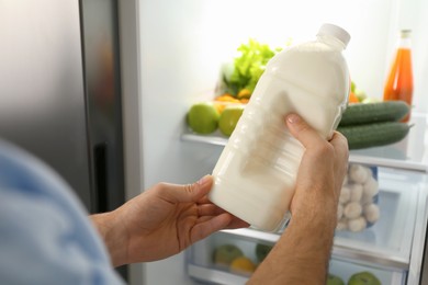 Man putting gallon of milk into refrigerator indoors, closeup