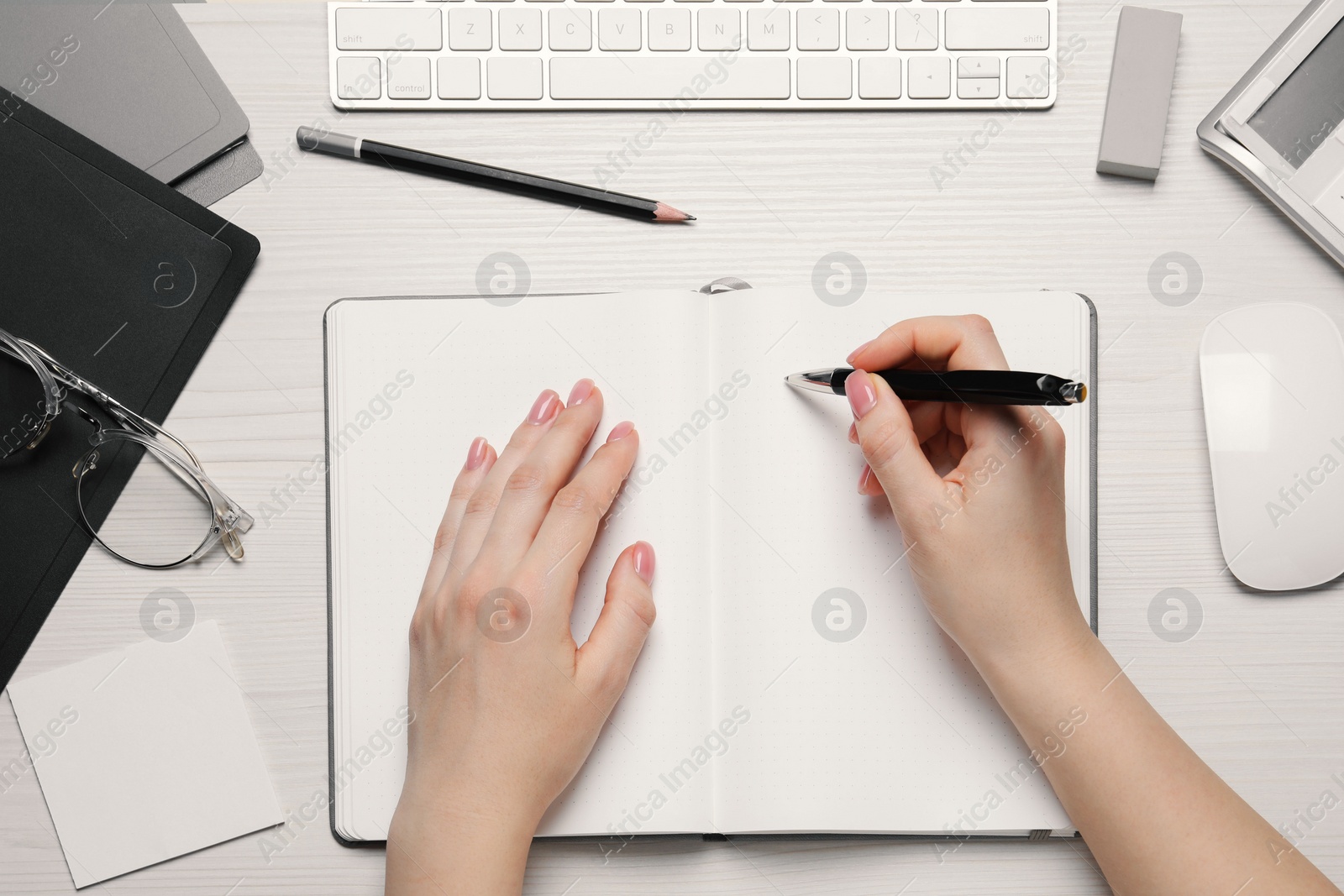 Photo of Woman writing in notebook at white wooden table, top view