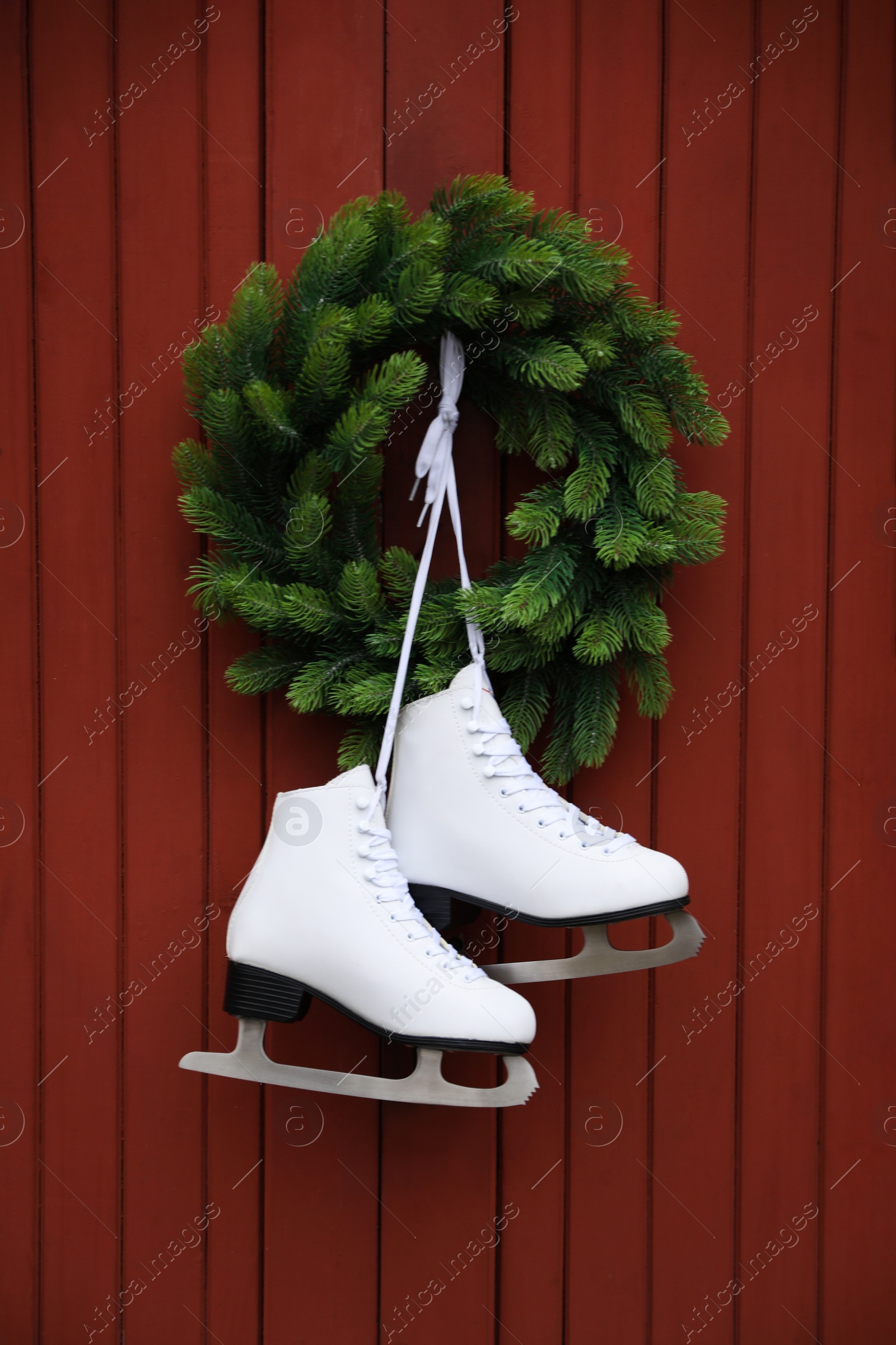 Photo of Pair of ice skates and beautiful Christmas wreath hanging on red wooden wall