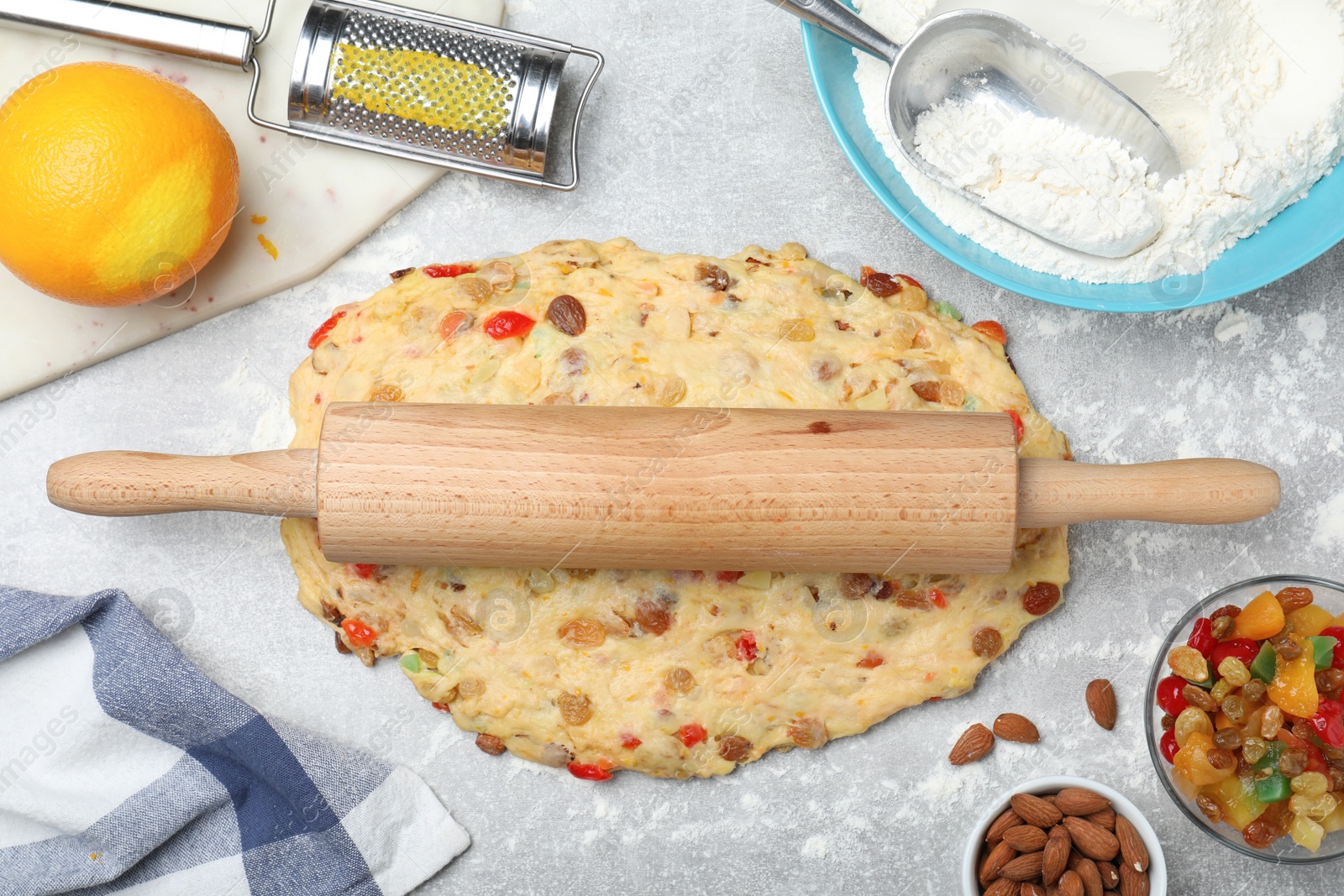 Photo of Raw dough for Stollen with rolling pin surrounded by ingredients at grey table, flat lay. Baking traditional German Christmas bread