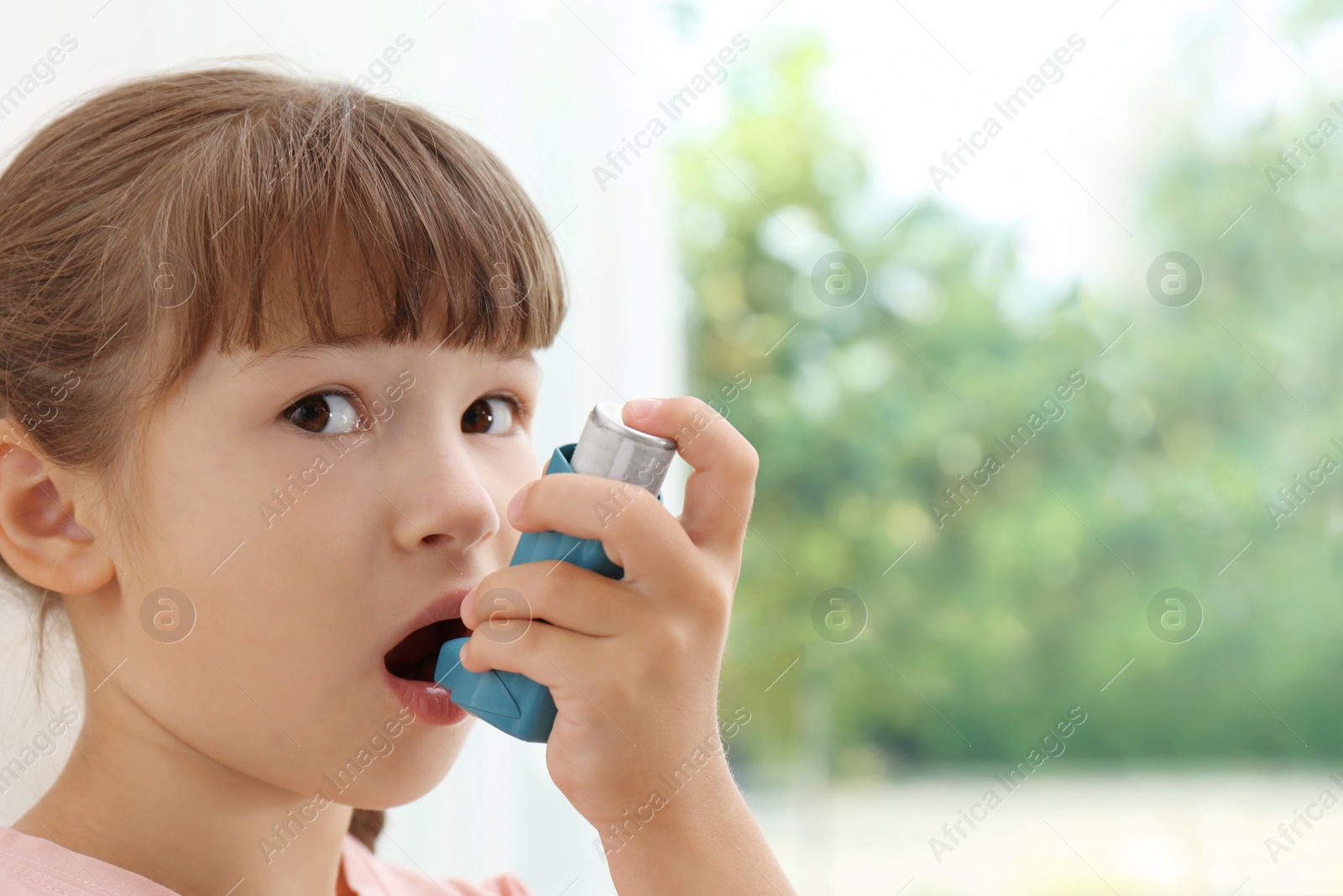 Photo of Little girl using asthma inhaler on blurred background