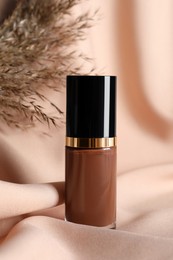 Photo of Bottle of skin foundation and dried reed on beige cloth. Makeup product