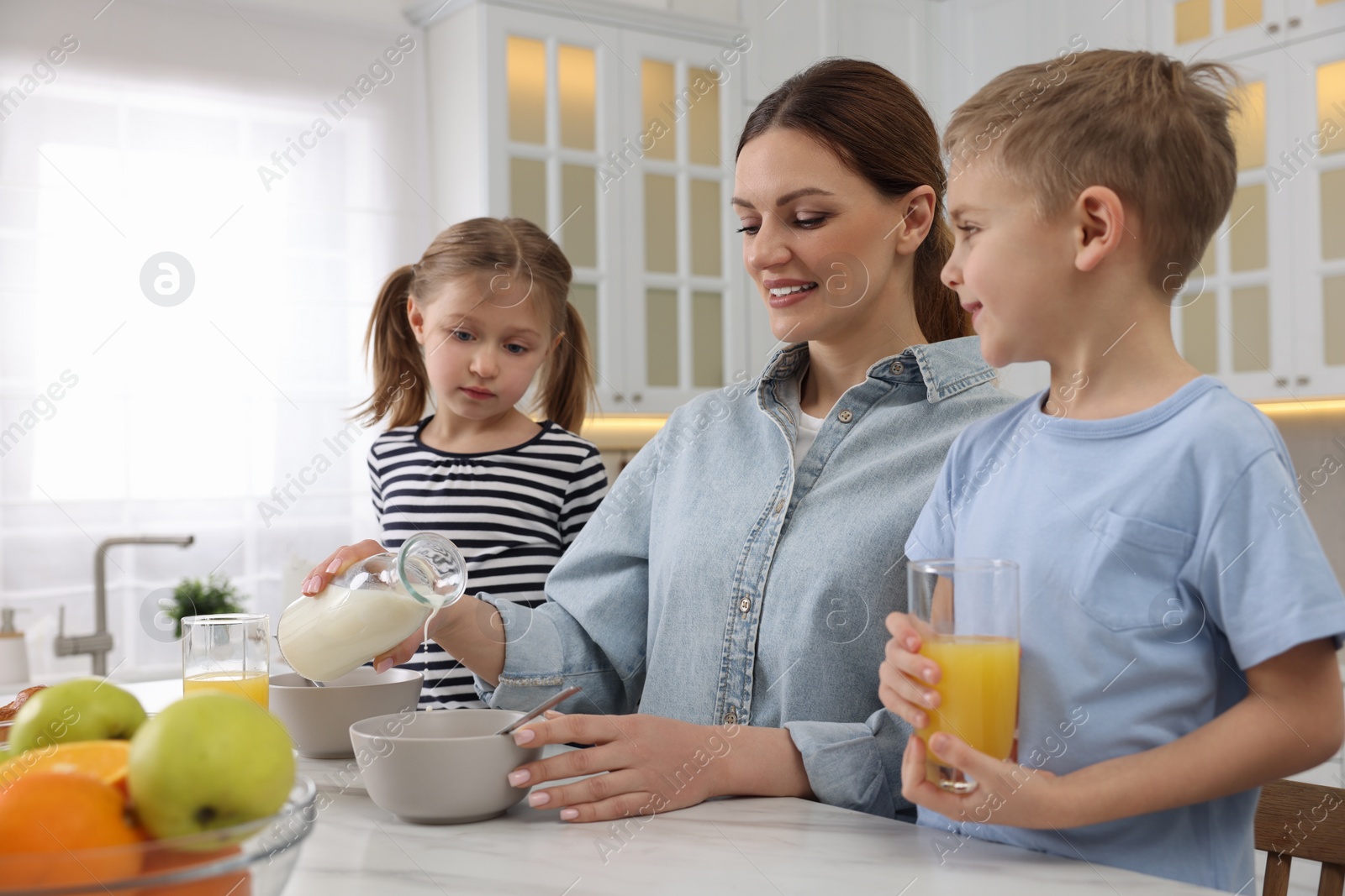 Photo of Mother and her little children having breakfast at table in kitchen