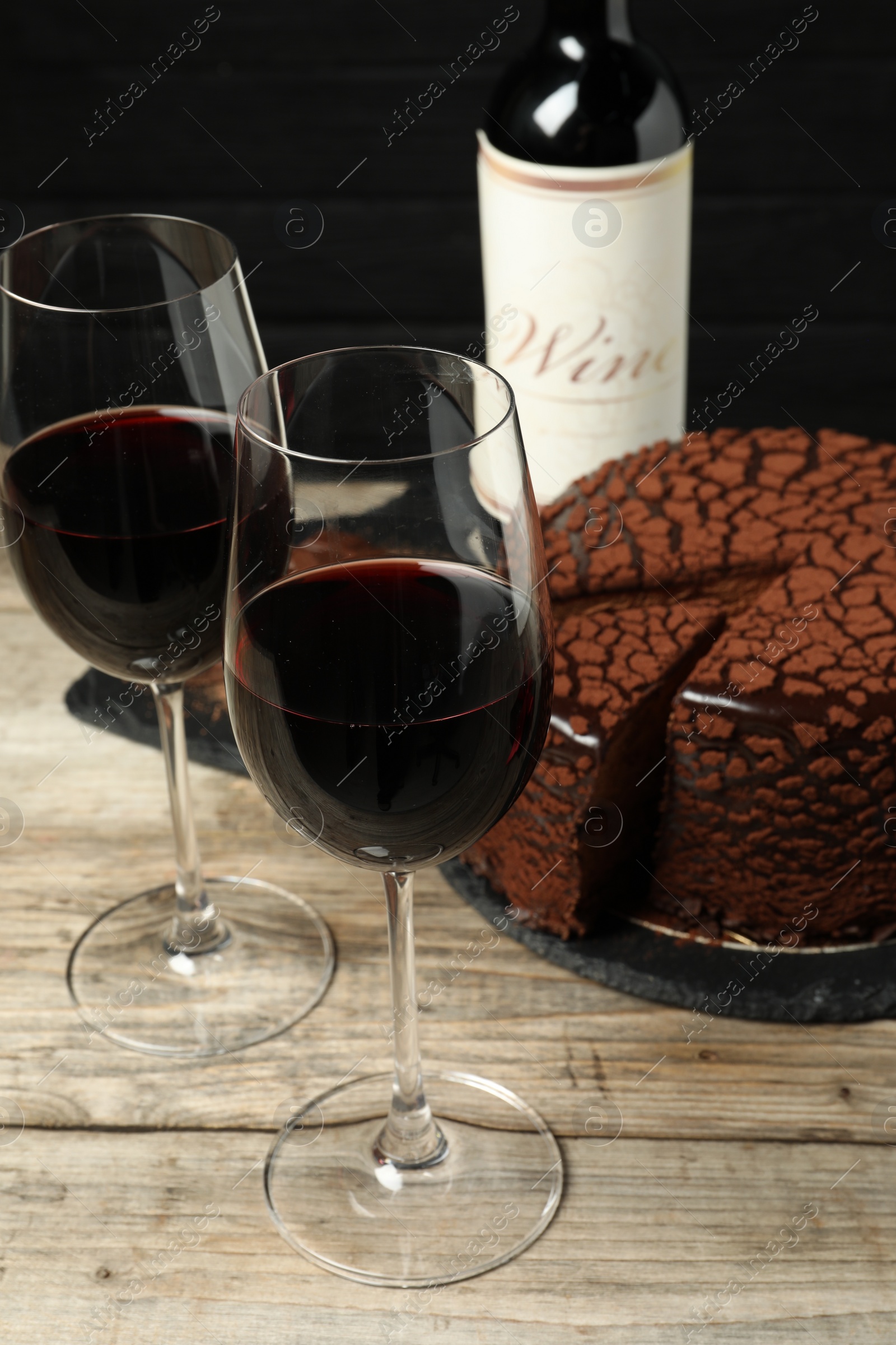 Photo of Delicious chocolate truffle cake and red wine on wooden table