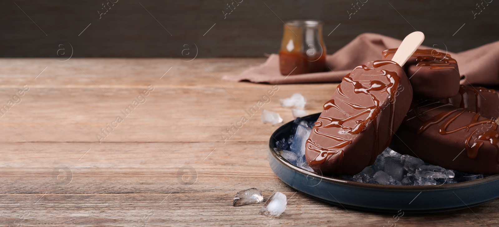 Image of Delicious glazed ice cream bars and ice cubes on wooden table, space for text. Banner design