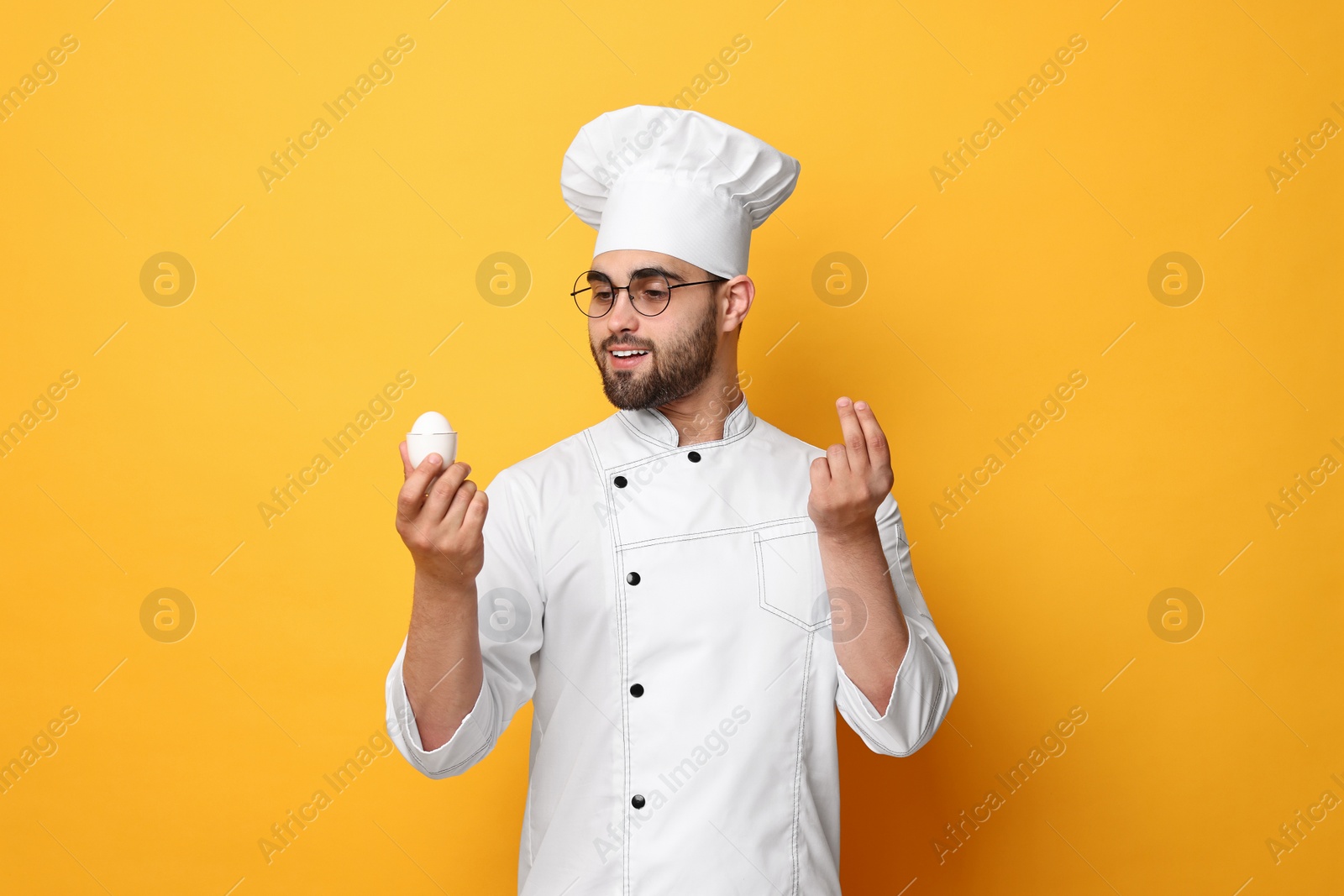 Photo of Professional chef holding egg and showing perfect sign on yellow background