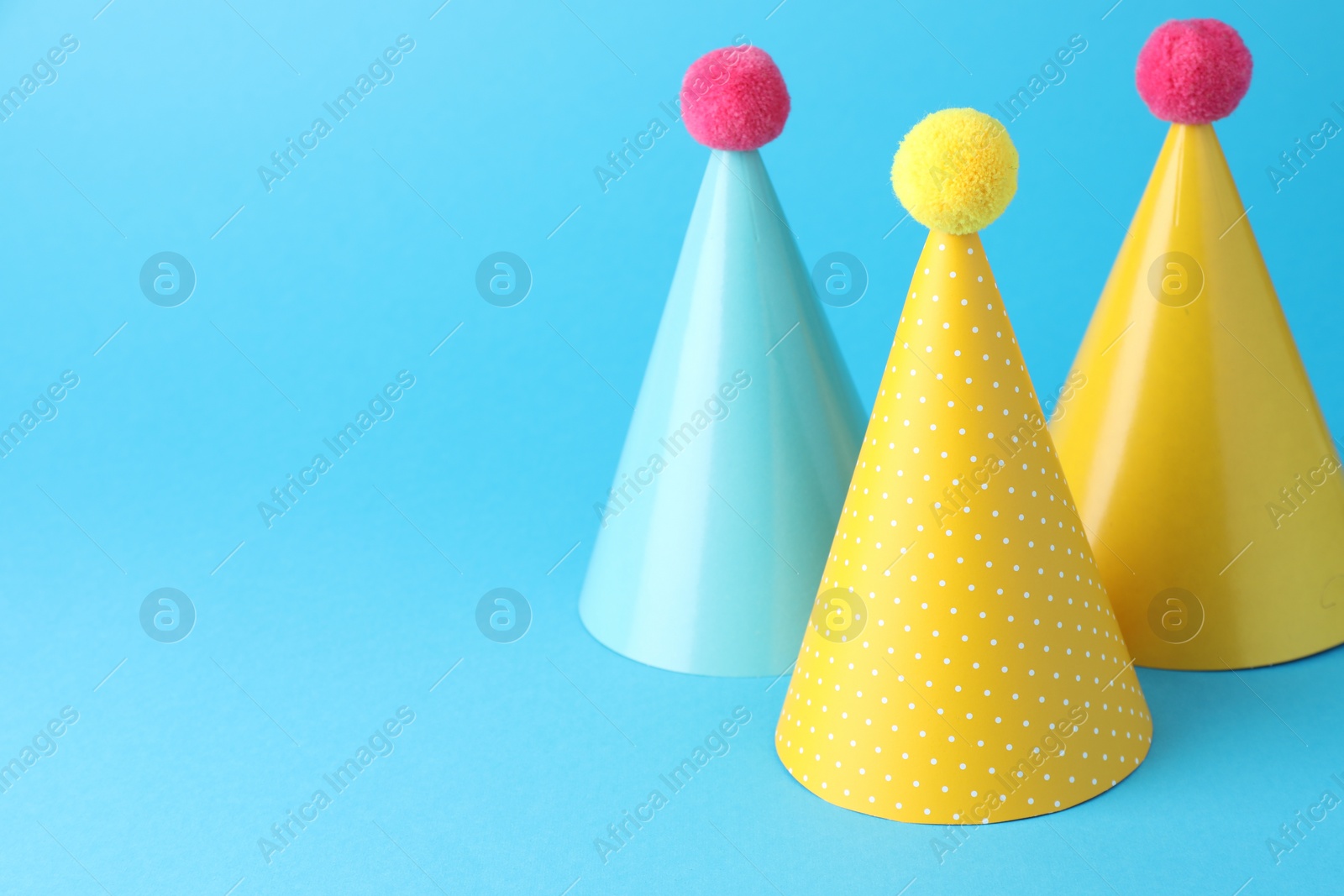 Photo of Colorful party hats on light blue background, space for text