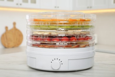 Photo of Dehydrator machine with different fruits and berries on white marble table in kitchen