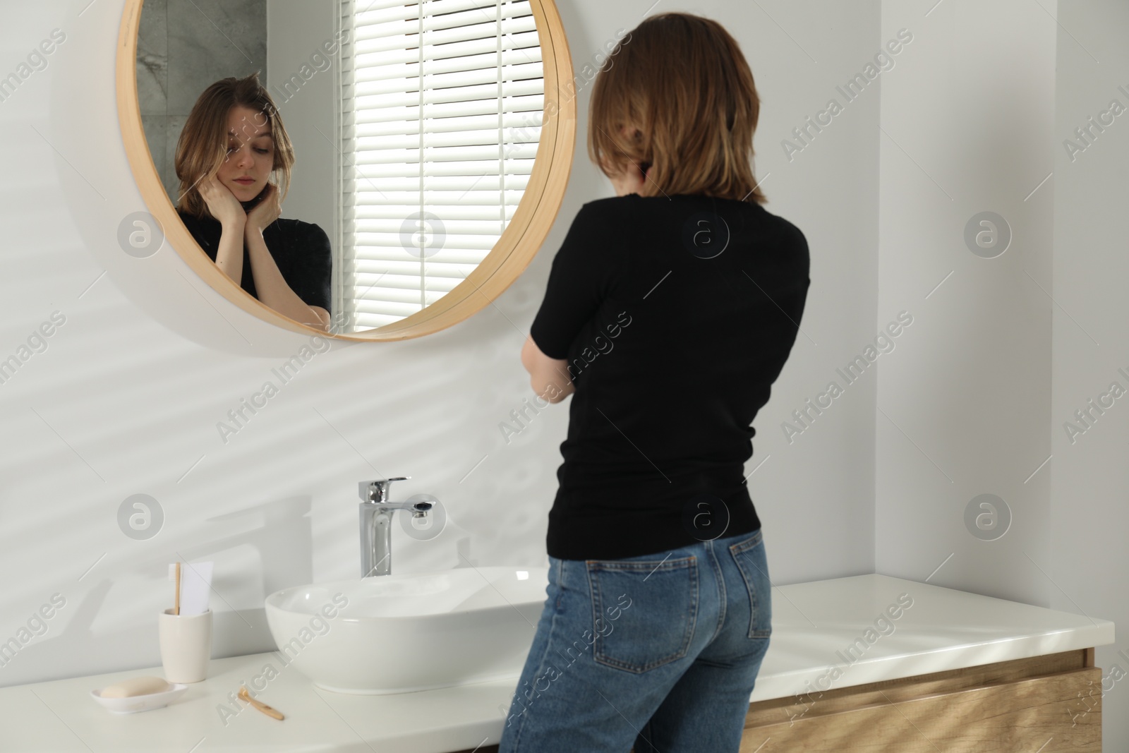 Photo of Sad young woman near mirror in bathroom