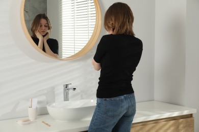 Sad young woman near mirror in bathroom