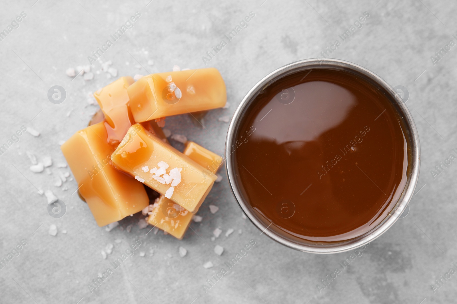 Photo of Yummy caramel candies, sauce and sea salt on grey table, top view