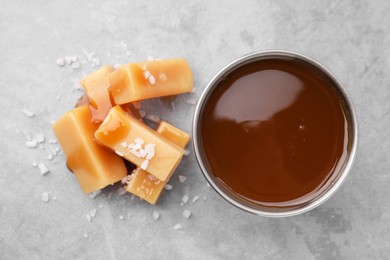 Yummy caramel candies, sauce and sea salt on grey table, top view