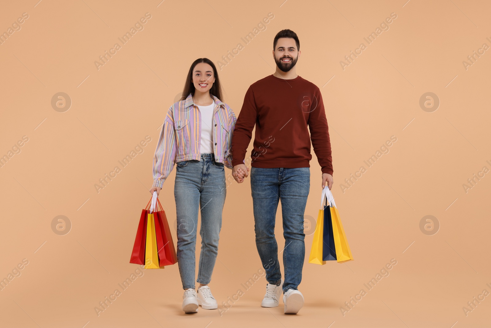 Photo of Happy couple with shopping bags on beige background