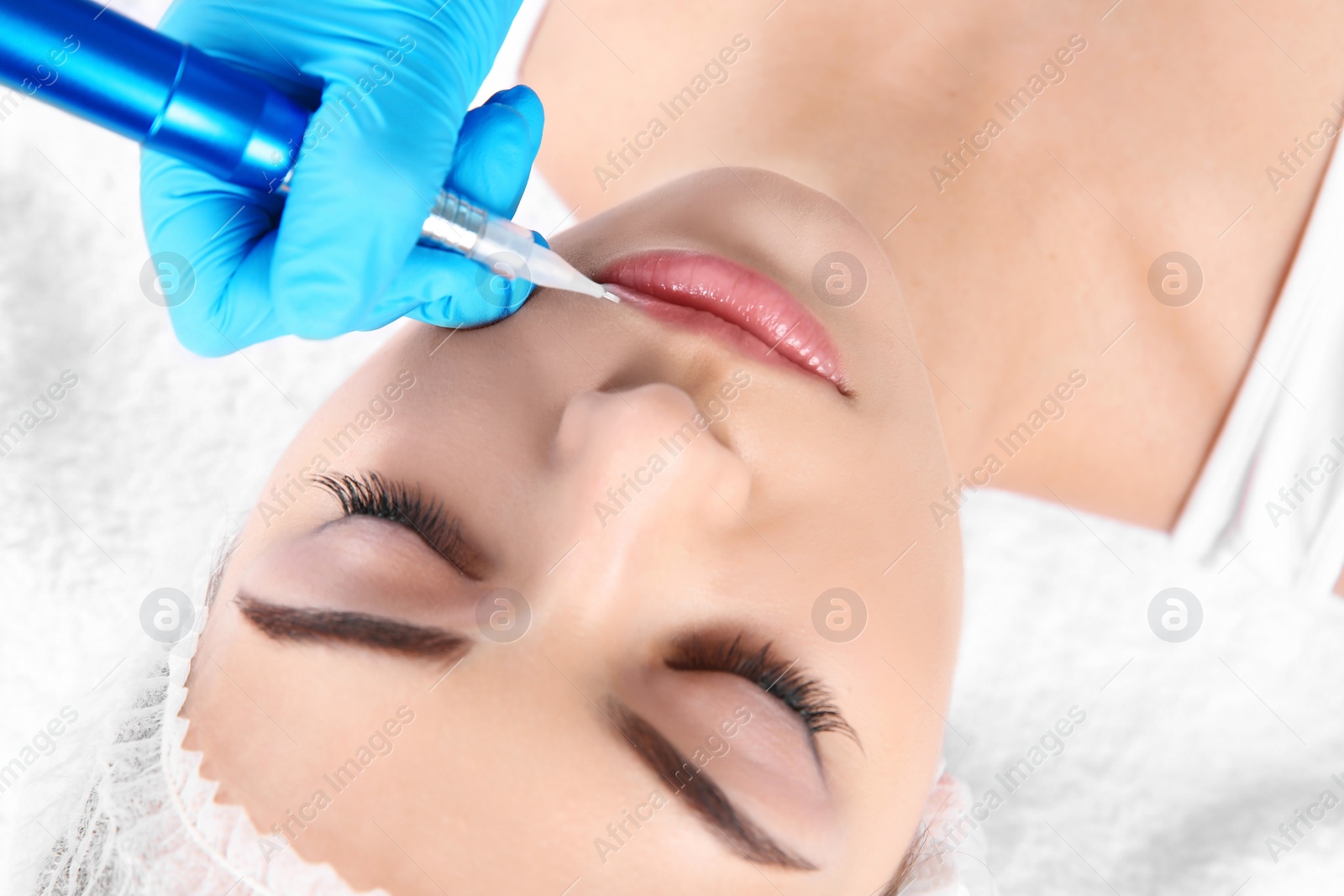 Photo of Young woman getting permanent makeup on lips in beautician salon, closeup