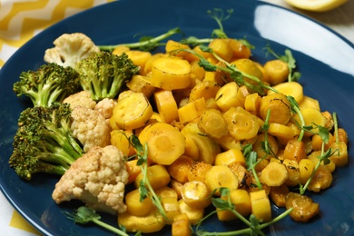 Photo of Tasty baked yellow carrot with broccoli, cauliflowers and pea sprouts on blue plate, closeup