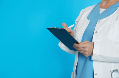 Mature doctor with clipboard on blue background, closeup. Space for text