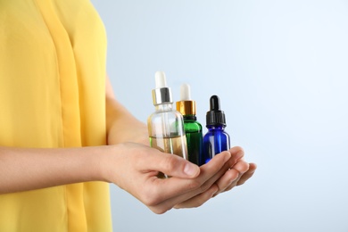 Woman holding bottles with essential oils on light background, closeup