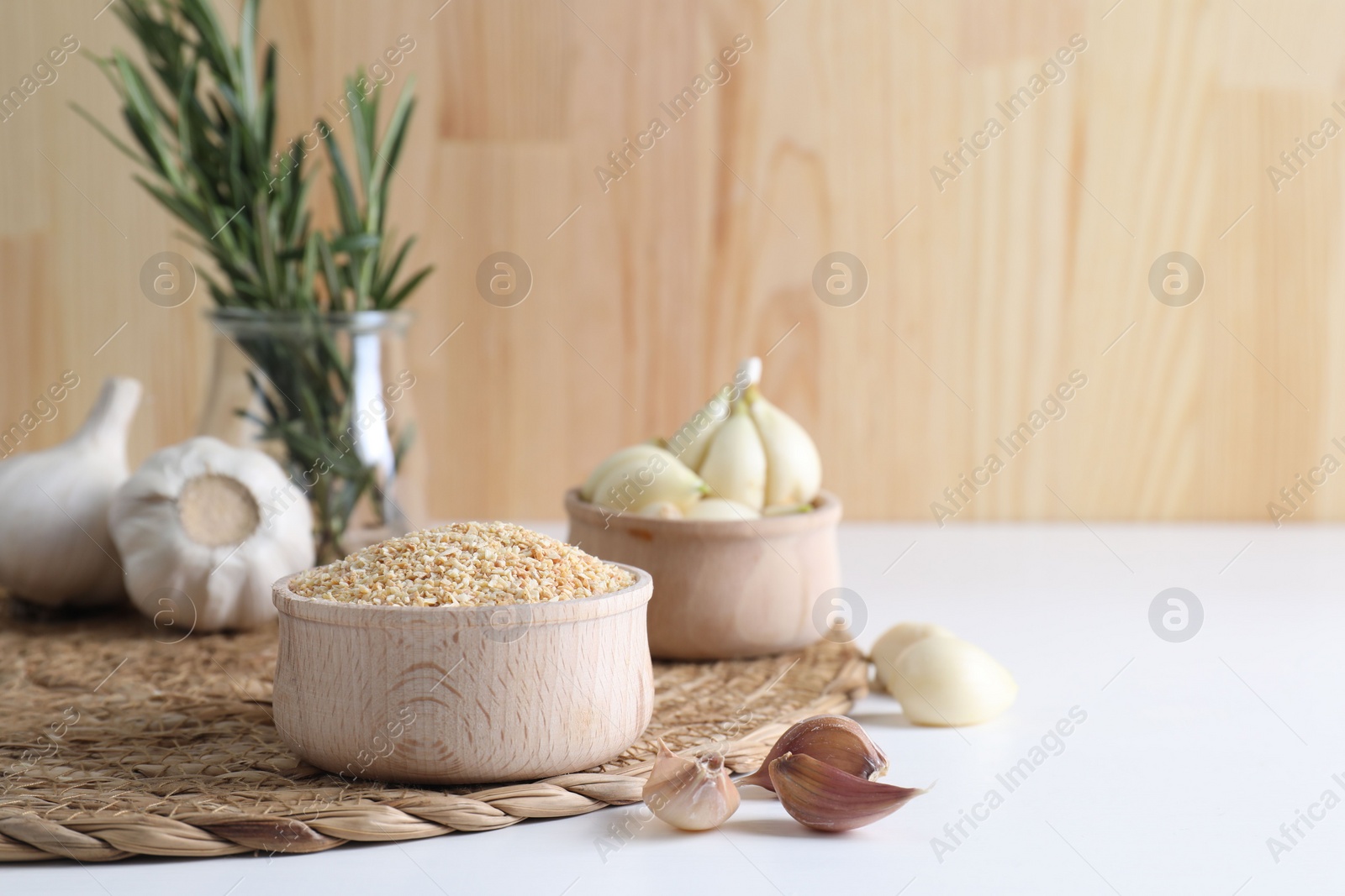 Photo of Dehydrated garlic granules in bowl, fresh bulbs and cloves on white table. Space for text