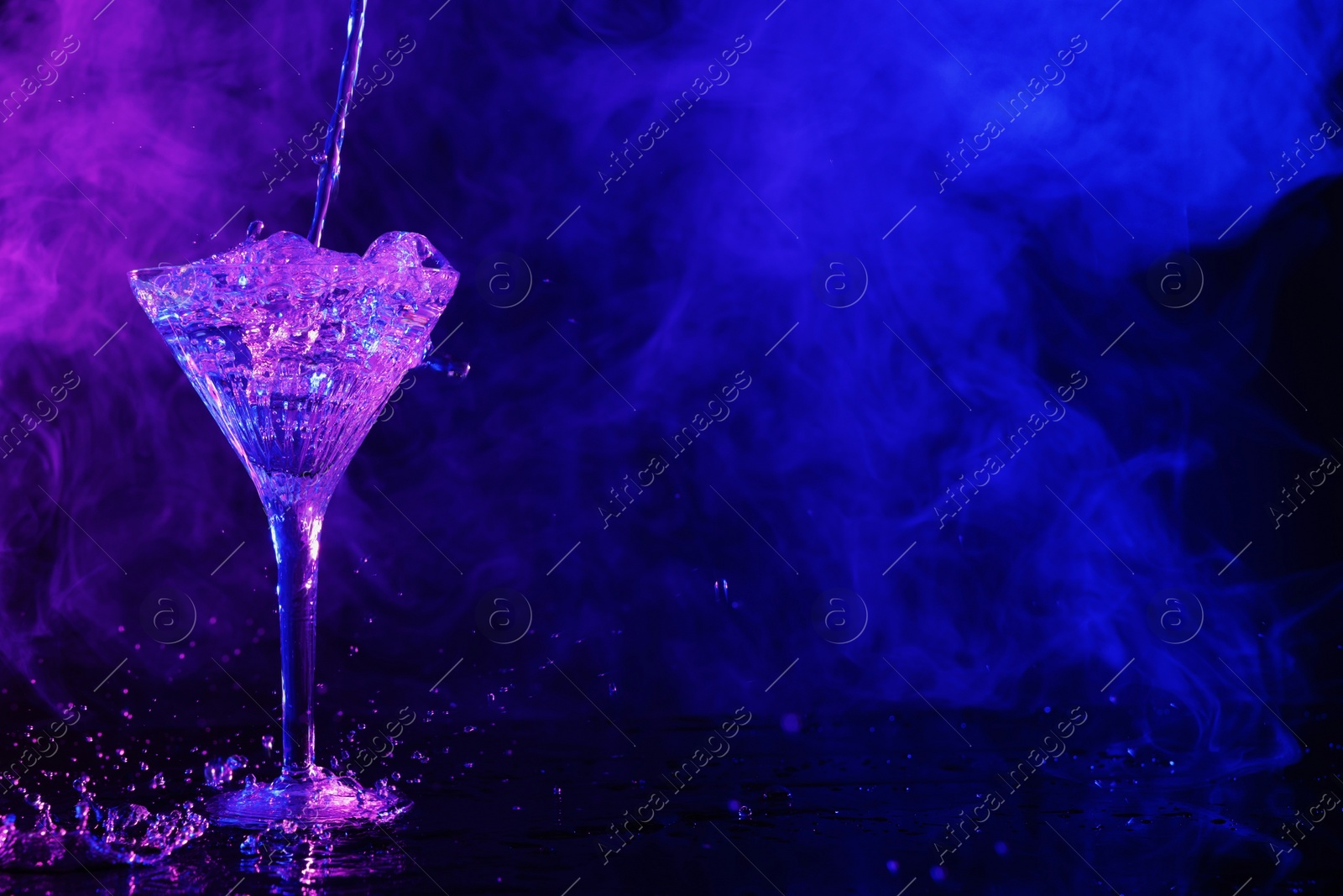 Photo of Pouring fresh martini into glass on table in neon lights, space for text
