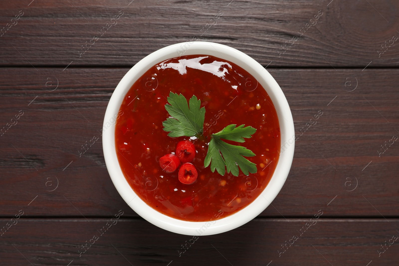 Photo of Spicy chili sauce with parsley on wooden table, top view