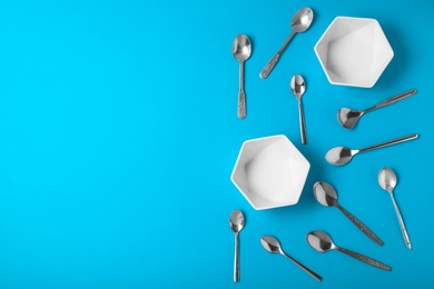 Flat lay composition with empty bowls and metal spoons on blue background, space for text