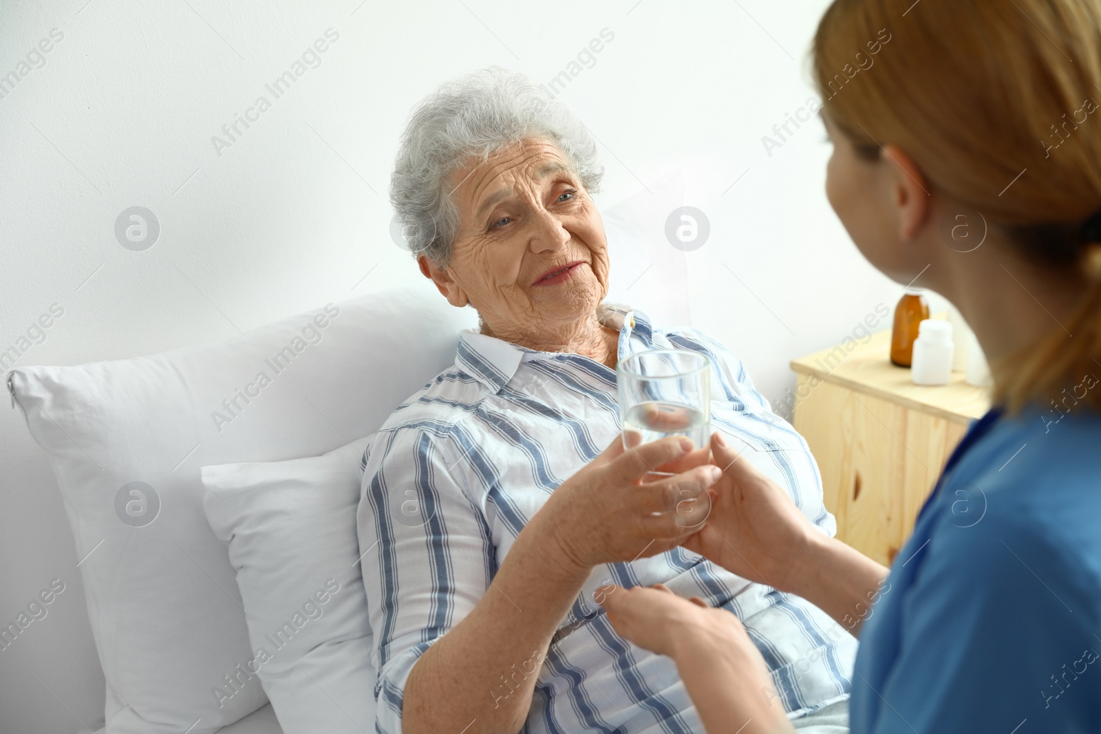 Photo of Nurse giving glass of water to elderly woman indoors. Medical assistance