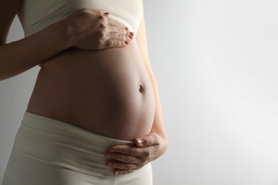 Pregnant young woman touching belly on light background, closeup. Space for text