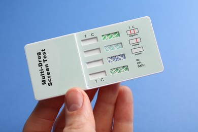 Woman holding multi-drug screen test on blue background, closeup