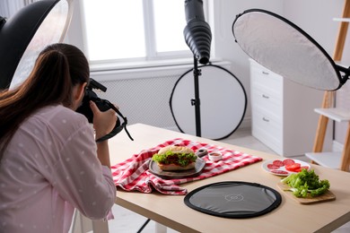 Young woman with professional camera taking photo of sandwich in studio. Food photography