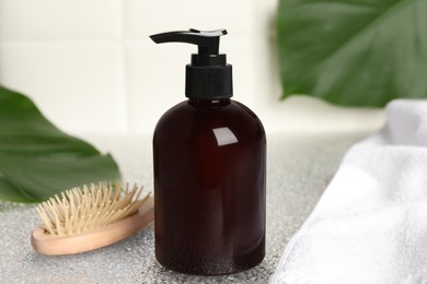 Photo of Shampoo bottle, hair brush, towel and green leaf on light table