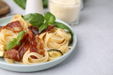 Photo of Tasty pasta with bacon and basil on light grey table, space for text