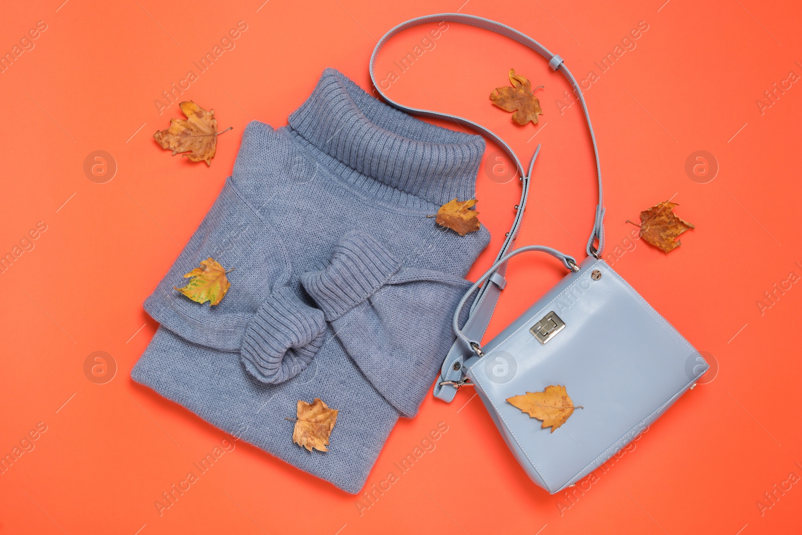 Photo of Warm sweater, bag and dry leaves on orange background, flat lay. Autumn season