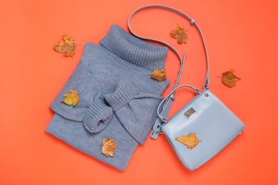 Photo of Warm sweater, bag and dry leaves on orange background, flat lay. Autumn season