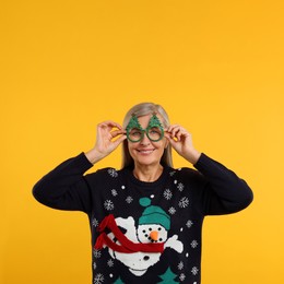 Photo of Happy senior woman in Christmas sweater and funny glasses on orange background