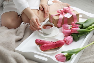 Photo of Tasty breakfast served in bed. Woman with tea, eclairs, gift box, flowers and I Love You card at home, closeup