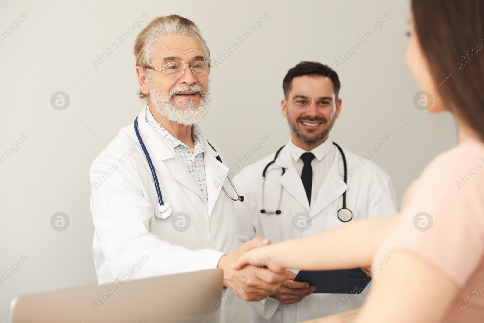 Photo of Happy senior doctor shaking hands with patient in clinic