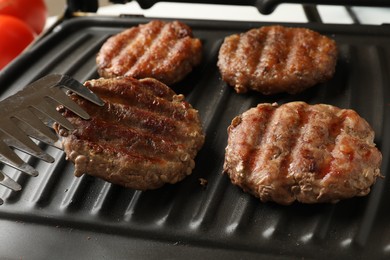 Photo of Taking delicious hamburger patty with tongs from electric grill, closeup