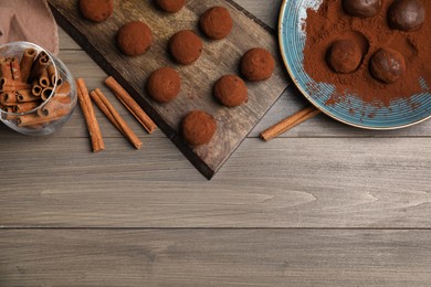 Photo of Delicious chocolate truffles with cocoa powder and cinnamon on wooden table, flat lay. Space for text