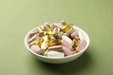 Photo of Different vitamin pills in bowl on olive background