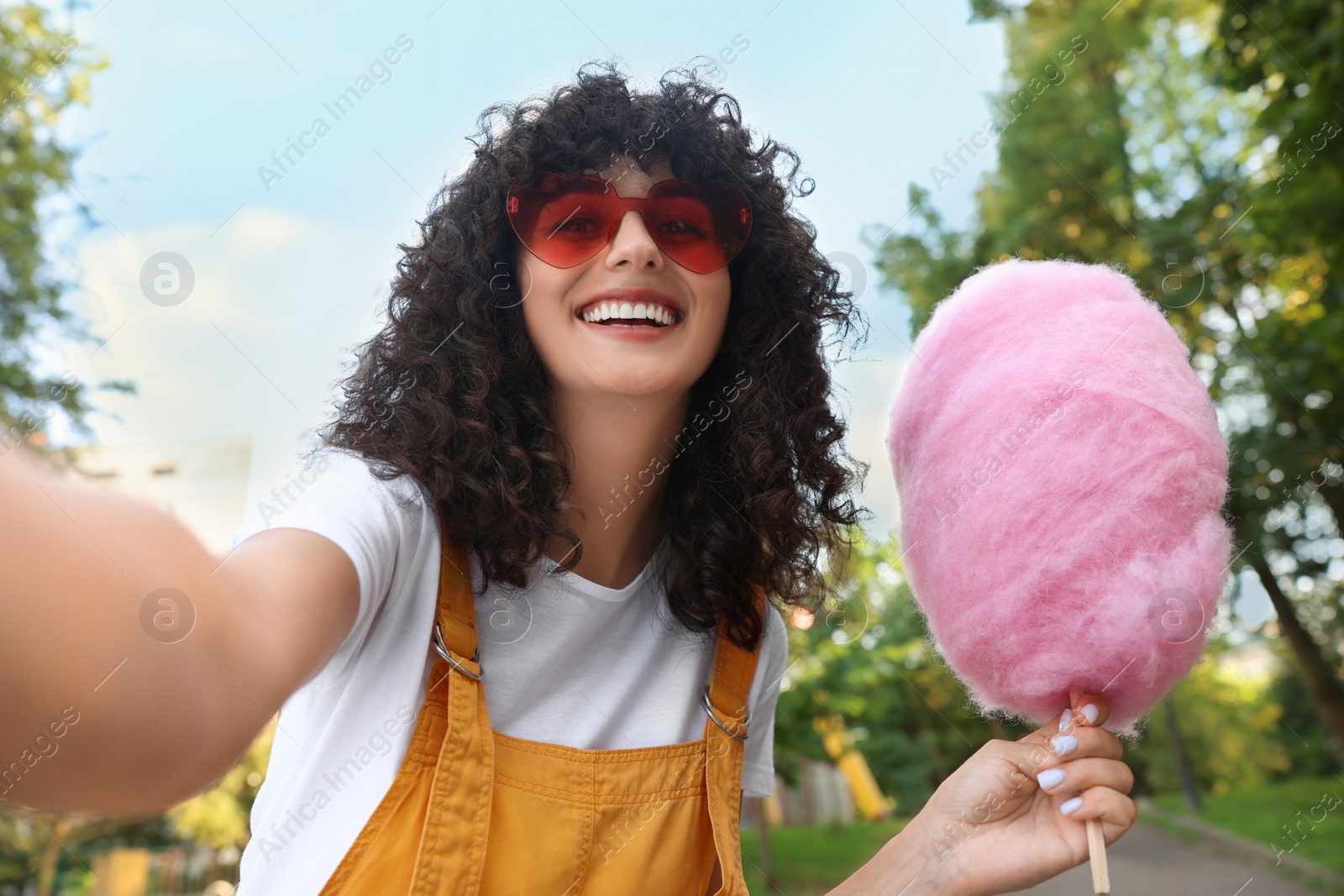 Photo of Happy woman with cotton candy taking selfie at funfair